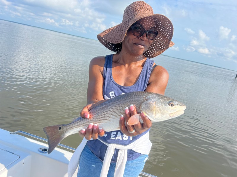 Person in a sun hat holds a fish on a boat with water and sky in the background.